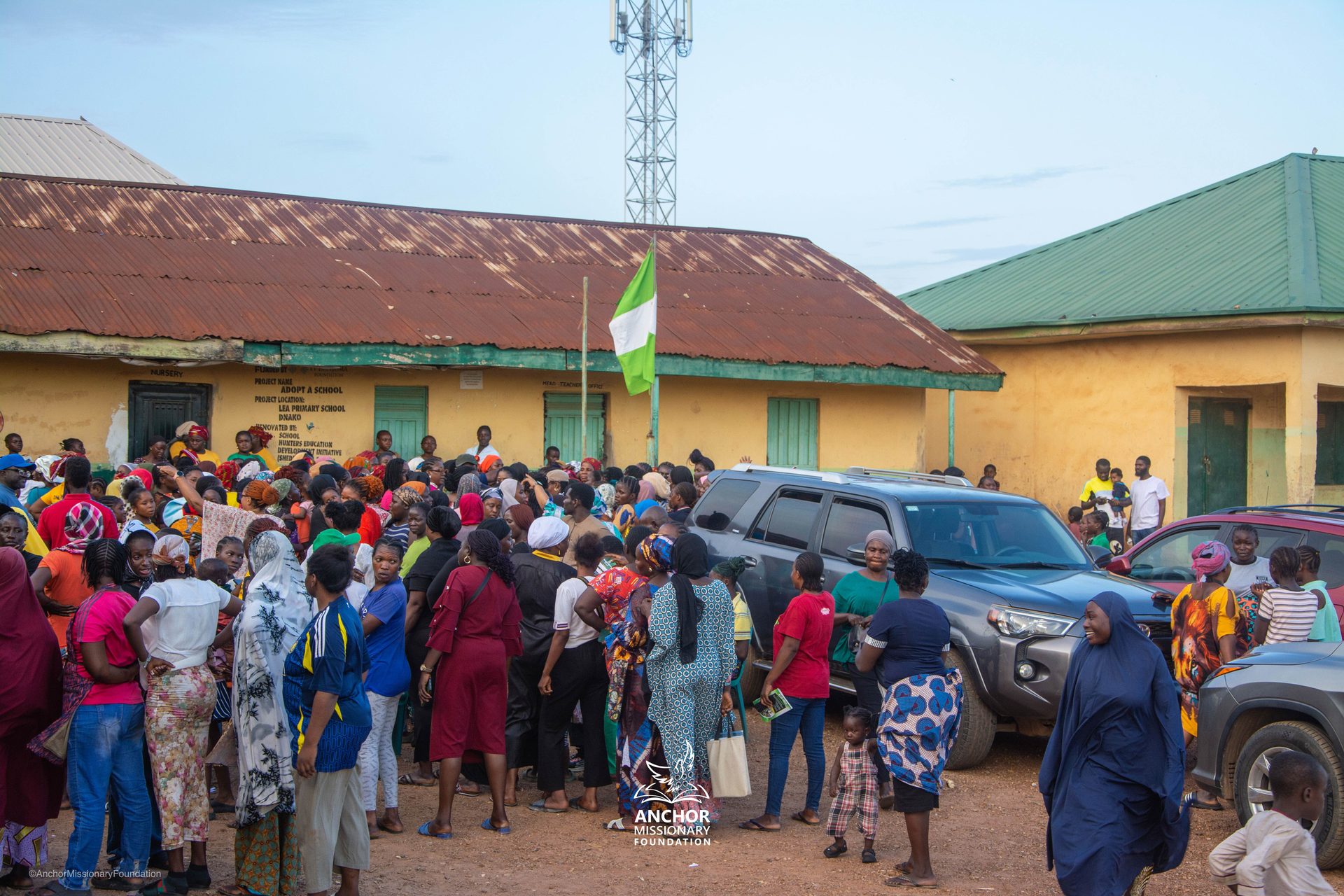 Community gathering outside a school building at dusk during an Anchor Missionary Foundation outreach in Abuja